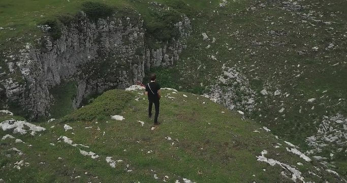 Dolly shot around a man playing electric guitar, top of a small cliff, aerial