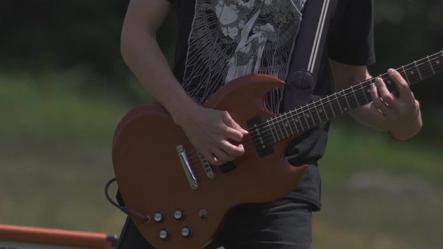 Close up on a man playing music on his electric guitar outdoor at a festival