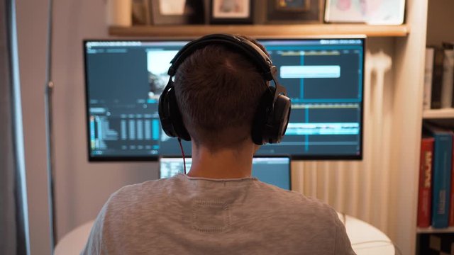 View from behind of a young video editor putting his headphones on before start working