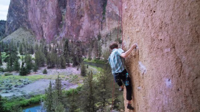Wide shot of young male climbing arete edge in Smith Rock's cliff wall