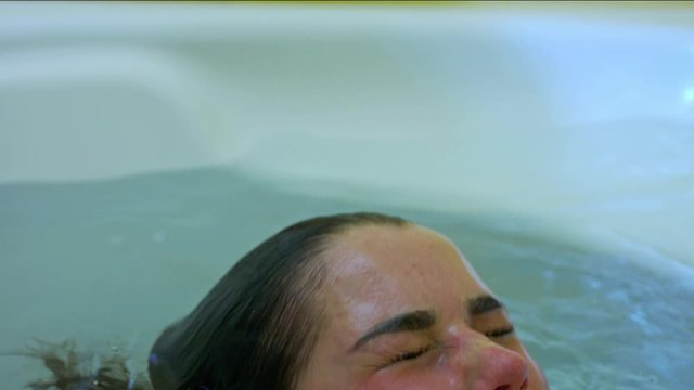 The young woman was submerged under water. I dive in the bathtub. A wet woman emerged from the water. Water flows down her face, hair and skin. Relax in the home bathroom.