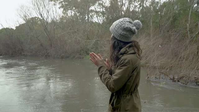 Beautiful girl rubbing her cold hands at the bank of river, profile shot
