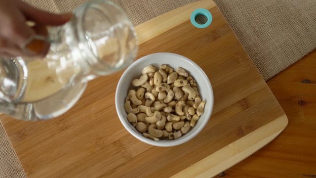 Woman pouring water into a bowl full of cashews