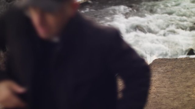 Full shot of male adult hiker climbing rock ledge from streaming river