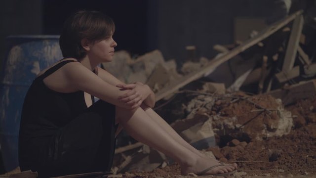 Young woman in an evening dress sitting in the dark in an abandoned building site