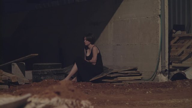Young woman in an evening dress anxious in the dark in an abandoned building site