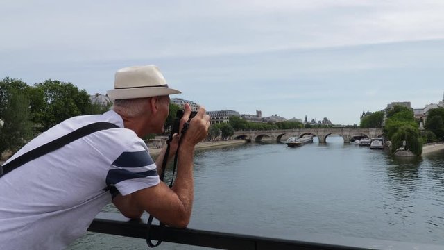 Middle aged man taking photos on the pont des arts bridge of ile de la cit&eacute; and seine river in paris on summer day, wide arc shot
