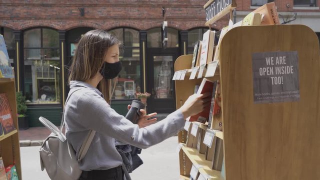Woman with mask picking books on sunny day at outdoor bookstore in Portland