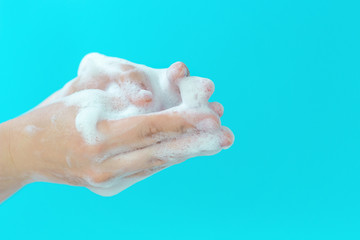The girl washes her hands with foam on blue background, side view