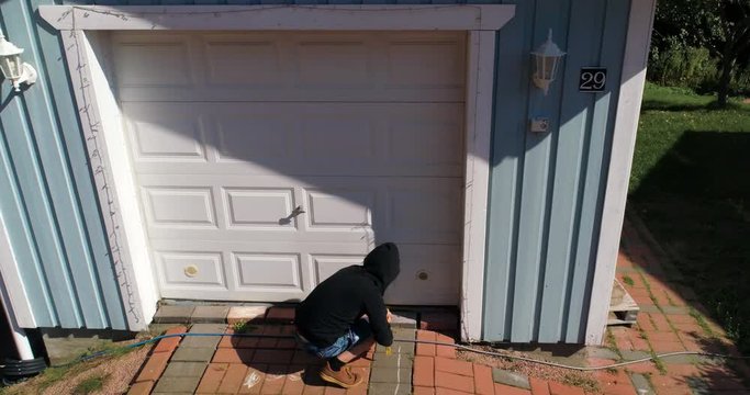 Aerial rising, drone shot tilting towards a thief, tryingto break in to a garage, with a crowbar, on a sunny, summer day, in Finland