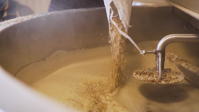 Male Brewery Worker Pouring A Sack Of Malt Into The Milling Tank - close up slowmo