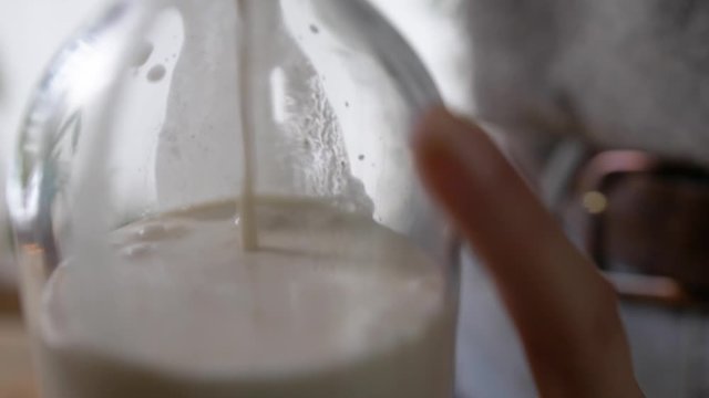 Woman Pouring Cashew Milk into a glass bottle