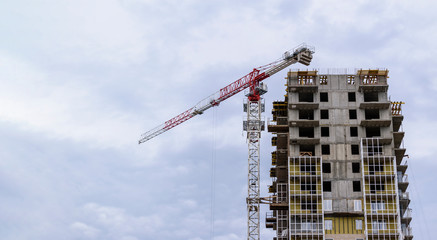 Naklejka premium Reinforced concrete house construction. High-rise construction crane. Sky with clouds. Multi-storey building construction concept. 