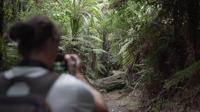 Young man with camera and backpack runs through forest in New Zealand