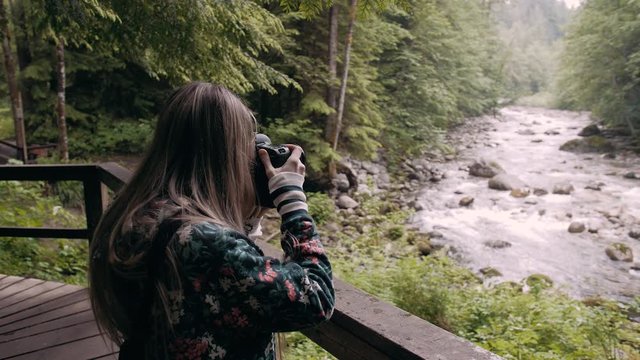 Slow motion shot of a female photographer taking photos of a river in Vancouver Lynn valley, Canada