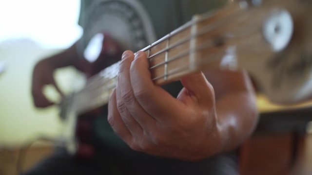 Male musician plays bass guitar at home studio. Close up at left hand and maple fretboard 4K