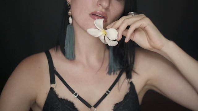 Pretty brunette woman touching her face with a white flower, sensually moving from one cheek to another