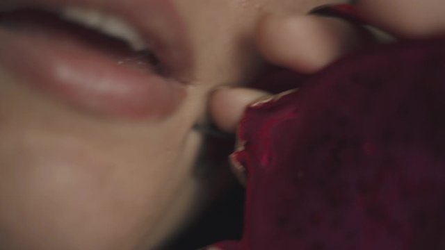 Close up portrait of pretty brunette woman with natural make up seductively licking ripe juicy piece of dragon fruit or pitaya