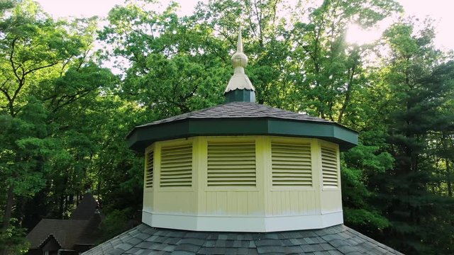 Ornamental cupola on a shingle roof, dramatic summer light shines through trees