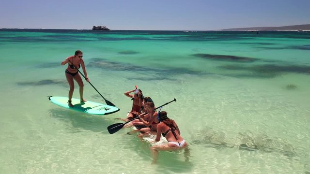 Happy group of young friends having fun sitting on large paddle board on water