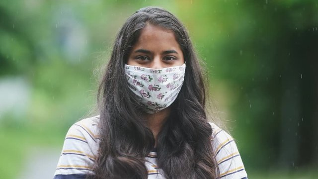 Pretty young dark skinned Indian girl black hair brown eyes standing in monsoon rain wearing cloth Mask for covid 19 slow motion