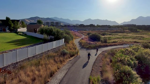 Couple riding bicycles along a nature pathway between a golf course and a river - aerial view