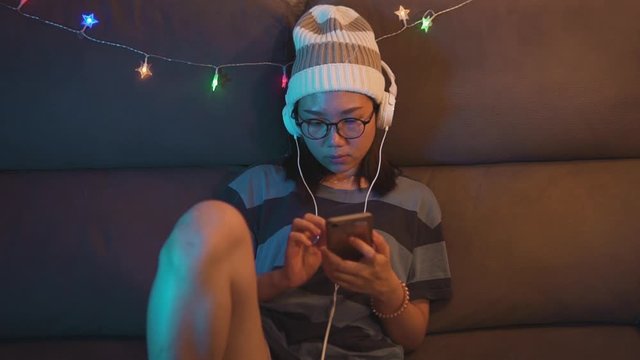 Young woman with headphones checking her social media apps on her smart phone. Stay conected online with friends during coronavirus pandemic quarantine. Using touch screen technology on cell phone.