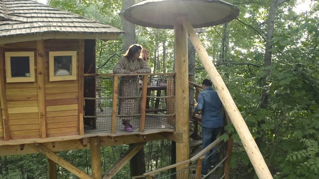 Pedestal 4k shot of a man walking up the stairs of a luxurious treehouse in a forest in Doln&iacute; Morava, Czechia, carrying a basket with breakfast, wife watching from upstairs. A couple in a treehouse.