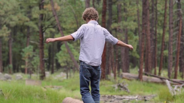 Young man steps up onto pipe and walks away from camera with arms out for balance
