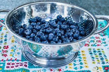 Blueberries in a stainless steel colander on brightly colored vintage tablecloth