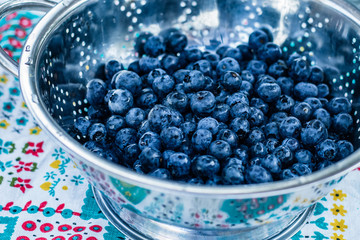 Blueberries in a stainless steel colander on brightly colored vintage tablecloth