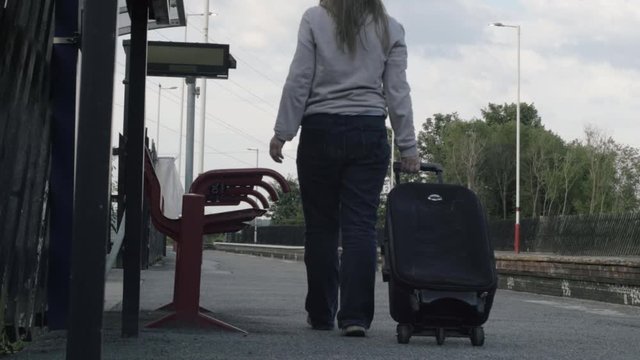 Woman wheels suitcase on train platform wide shot