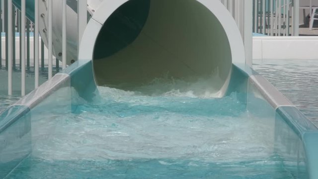 A little girl laughs as she slides out the bottom of a tube slide at a waterpark.