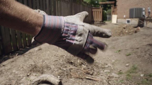 Man puts on work gloves in wood fenced dirt and debris covered yard