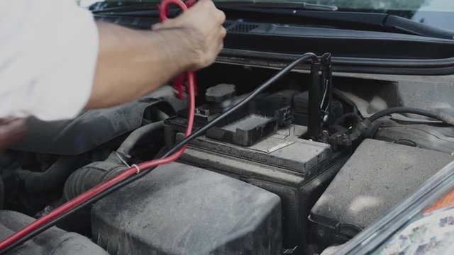 Man attaches booster cables to car battery then removes them. The engine block is not clean