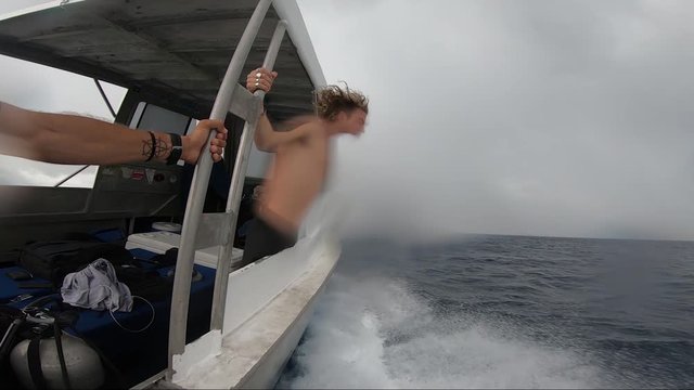 A young man with long blonde hair holds on to the metal frame of the boat as strong waves and winds hits the boat during a stormy day in Madang, Papua New Guinea on a diving trip.