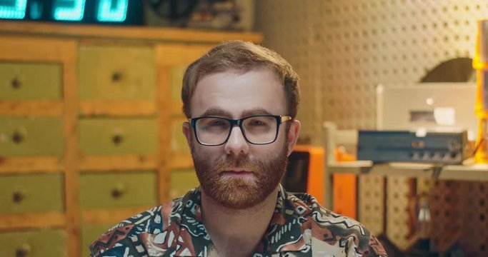 Portrait of young Caucasian man in glasses looking straight too camera with sad shrewd eyes in vintage style. Retro interior. Close up of male nerd with upset serious face.