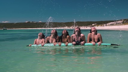 Pretty young girls lying on surfboard throwing hairs into air during beautiful sunny day at Hamelin Bay