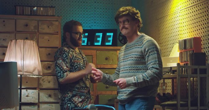 Two funny Caucasian friendly men nerds in glasses and old style clothes dancing and moving while listening to music of 70's. Vintage room of 80's. Retro males having fun at home.