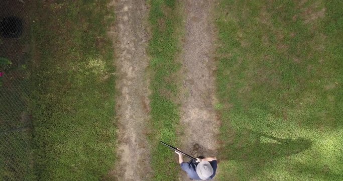 Low aerial view looking straight down on a man carrying a shotgun in the ready position walking into then out of the frame as he looks right then left.