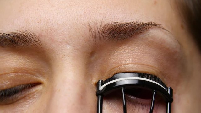 Woman uses eye lash curler on her lashes.