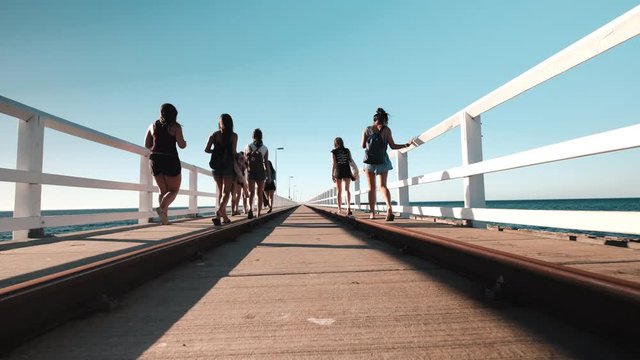 Girls walking on pier in Busselton jetty in Busselton, Western Australia. Low angle view on a rusty railway. Dolly backwards
