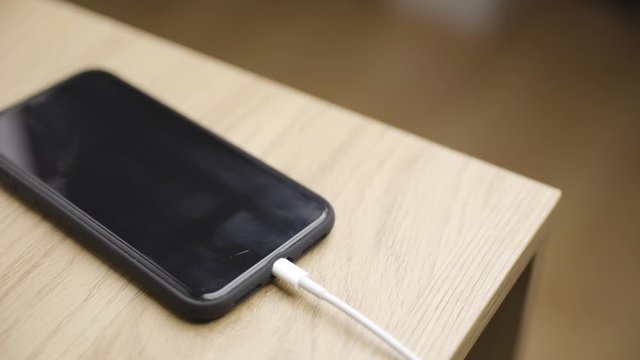Male hand connects charger to smartphone on table, unplugs, close-up