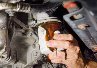 Close up of  a hand removing an oil filter on the underside of a car with oil dripping