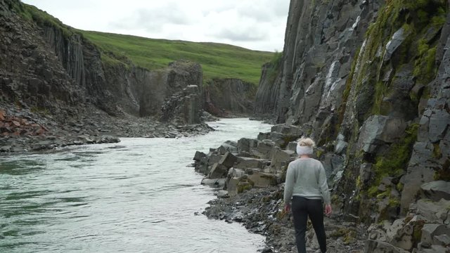 Young blonde girl walking across the riverbank of an emerald stream in an Icelandic landscape