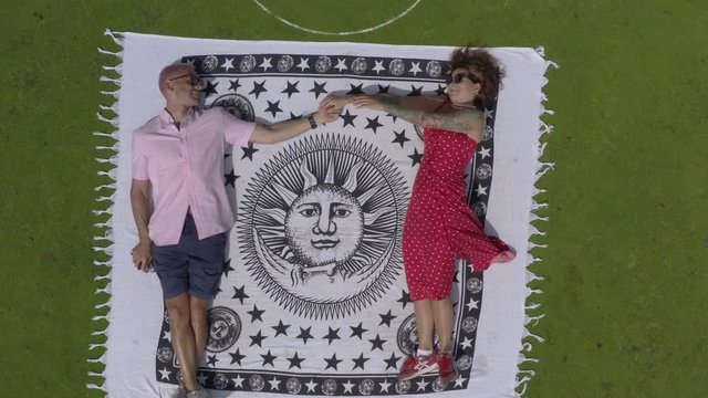 Overhead Zoom Out From An Attractive Male And Female Sitting On A Towel On The Putting Green Of A Gold Course.