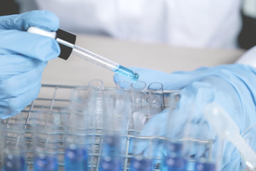 Scientists hold the pipette and drop the blue chemical liquid for research and analysis in a laboratory