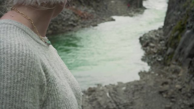 Beautiful young Caucasian woman wearing a woolen headband stares back at the emerald river in Iceland
