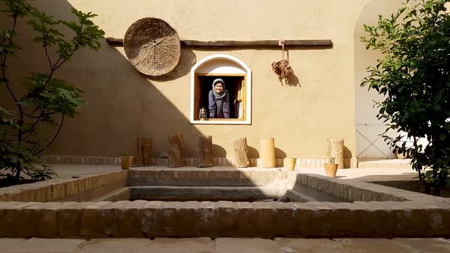A girl opens the wooden window and smile in an old house built with mud in a historical village in desert in Iran