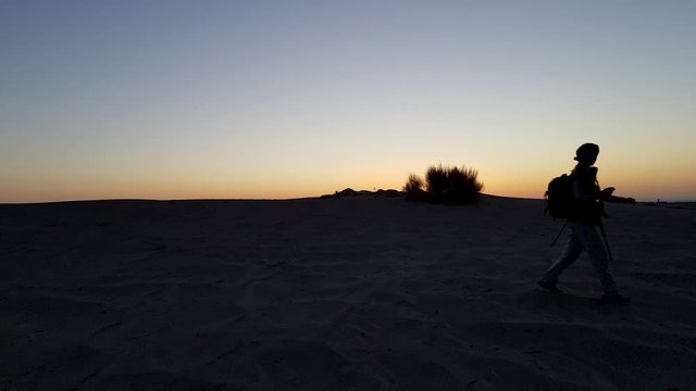 A girl walking on sand dunes in a desert area in early morning at twilight moments before sunrise in Iran, silhouette shot